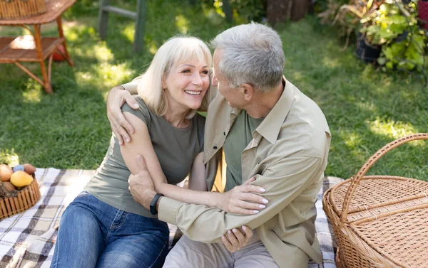 Emocionados cónyuges mayores haciendo picnic en el jardín, abrazando y riendo, sentados juntos en la manta al aire libre —  Fotos de Stock