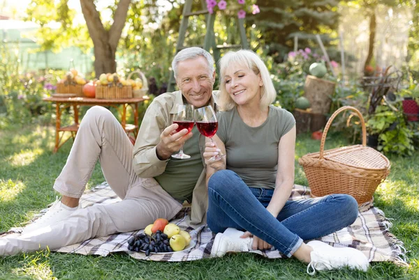 Szczęśliwej rocznicy. Kochający małżeństwo starsza para pije wino siedząc na kocu, mając piknik w ogrodzie — Zdjęcie stockowe