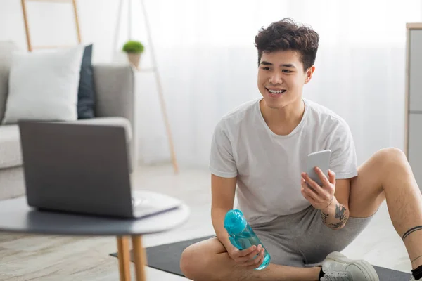 Азіатський хлопець займається вправами вдома і дивиться онлайн-уроки — стокове фото