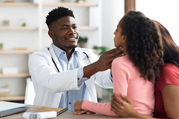 Médico afroamericano palpando la garganta de una niña en la clínica —  Fotos de Stock