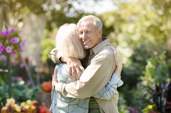 Kochająca starsza para przytulająca się podczas spaceru we własnym ogrodzie na wsi, ciesząca się wakacjami — Zdjęcie stockowe