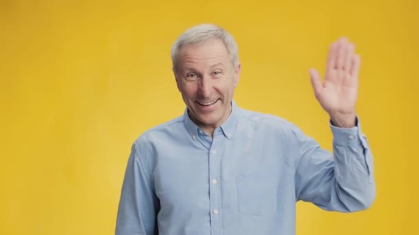 Bom dia. Feliz animado sociável sênior homem acenando mão para câmera e sorrindo, saudação alegremente, fundo amarelo — Vídeo de Stock