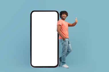 Büyük akıllı telefondan poz veren mutlu Hintli adam, başparmağını kaldırıyor.