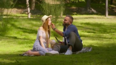 Romantik yaz buluşması. Mutlu çift yaz parkında piknik yapıyor, çilek yiyor ve öpüşüyorlar.