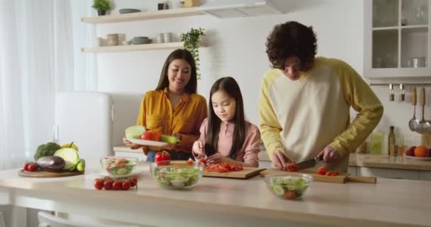 Bonito ásia menina corte vegetais no cozinha, ajudando pais com preparação jantar orgulhoso mãe beijá-la zoom no — Vídeo de Stock