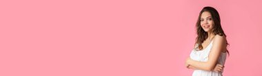 Pembe arka planda poz veren güzel, gülümseyen genç bir kadın.