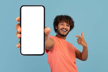 Havalı kıvırcık Hintli adam cep telefonunu boş ekranla gösteriyor.