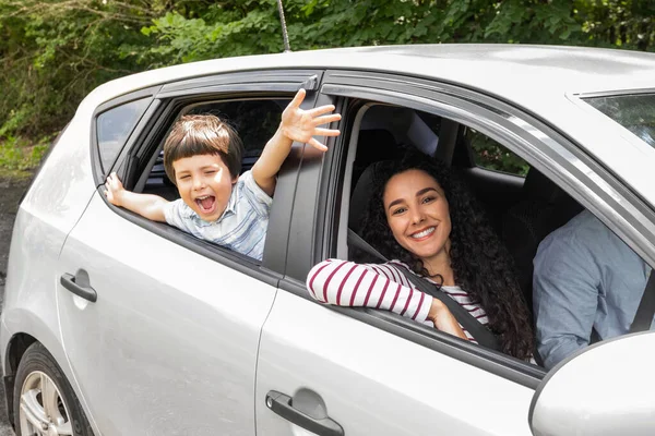 Feliz joven árabe hombre y mujer conduciendo coche, pequeño niño excitado con la boca abierta gesto, saludando con las manos en la ventana —  Fotos de Stock