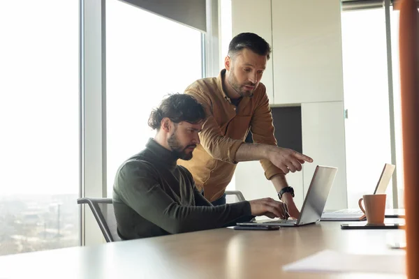 Två manliga kollegor arbetar tillsammans, diskuterar affärsidéer nära bärbar dator på öppet utrymme företagets kontor — Stockfoto