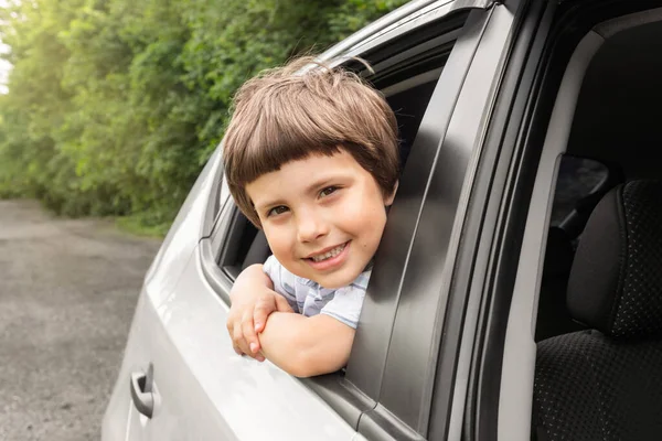 Petit garçon souriant roule en voiture, regarde par la fenêtre ouverte, s'amuser, profiter de la promenade en voiture, en plein air en été — Photo