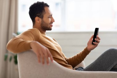 Evde akıllı telefon kullanan gülümseyen bir Arap portresi.