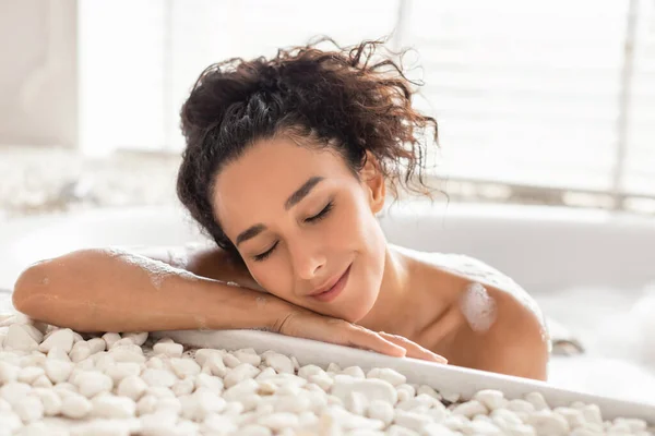 Wanita muda cantik berbaring di bubble bath dengan mata tertutup di rumah. Konsep kecantikan dan kesehatan — Stok Foto