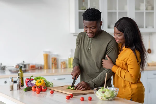 Jovem mulher negra olhando para o marido cozinhando salada na cozinha — Fotografia de Stock