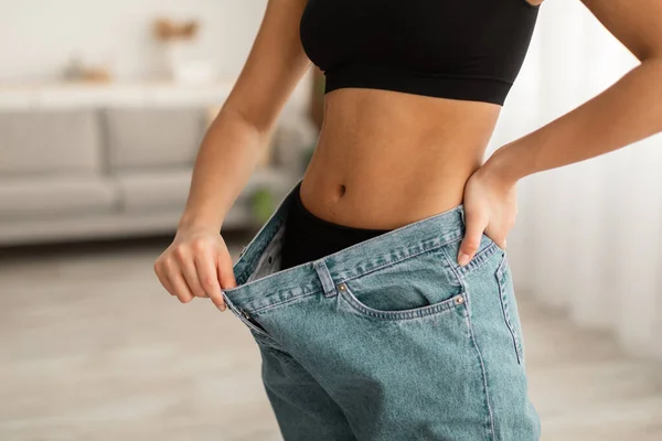 Senhora preta irreconhecível mostrando músculos abdominais vestindo jeans de grandes dimensões interior — Fotografia de Stock