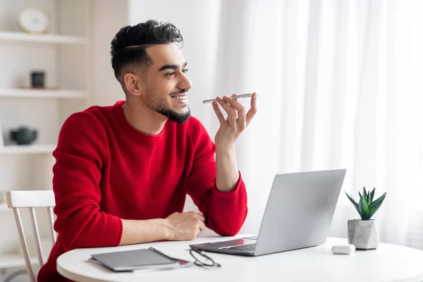 Lächelnder gutaussehender Millennial-Araber mit Bart in roter Kleidung telefoniert am Arbeitsplatz mit Laptop — Stockfoto