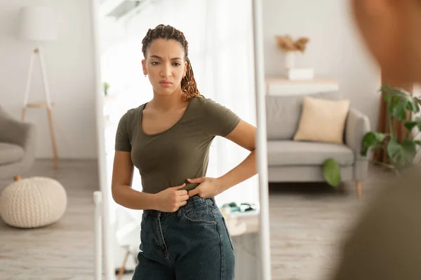 African Lady Touching Belly After Weight Gain Near Mirror Indoor