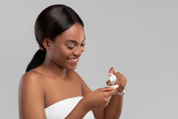 Heureuse femme afro-américaine millénaire attrayante appliquant de la crème ou de la lotion sur du coton — Photo