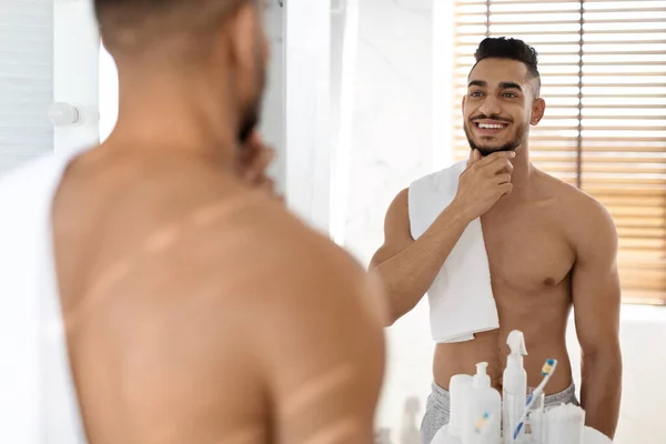 Hombre árabe guapo sin camisa con toalla en el hombro mirando en el espejo — Foto de Stock