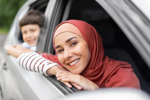 Vrolijke Midden-Oosten mooie vrouw in hijab en kleine jongen kijken in open raam in de auto, buiten in de zomer, close-up — Stockfoto