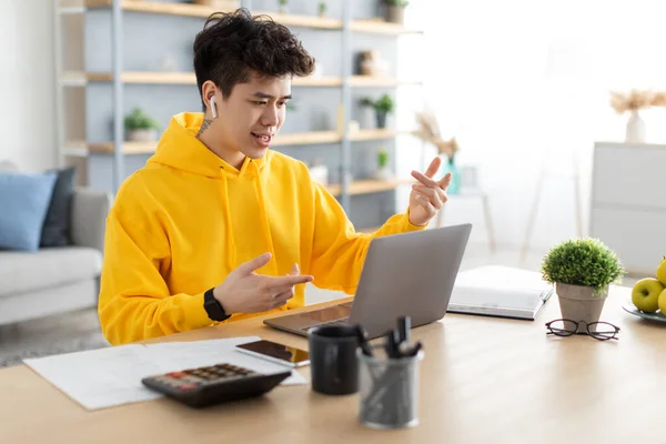 Hombre asiático usando portátil con auriculares sentados en el escritorio —  Fotos de Stock