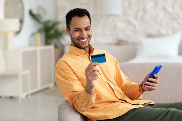 Sonriente usando teléfono y tarjeta de crédito en casa —  Fotos de Stock