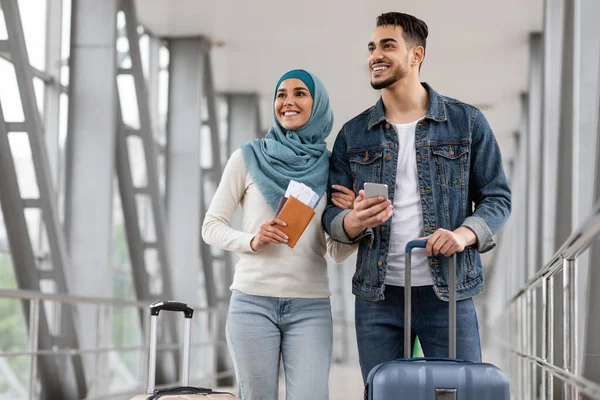 Gioioso sposi islamici in piedi con bagagli, passaporti e smartphone in aeroporto — Foto Stock
