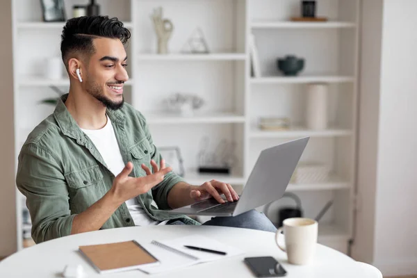 Lächelnd hübscher Millennial-Araber mit Bart und Kopfhörer am Arbeitsplatz mit Laptop zu Hause — Stockfoto