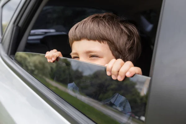 Веселий маленький хлопчик дивиться з відкритого вікна і насолоджується поїздкою з батьками в машині влітку, на відкритому повітрі, у вільному просторі — стокове фото
