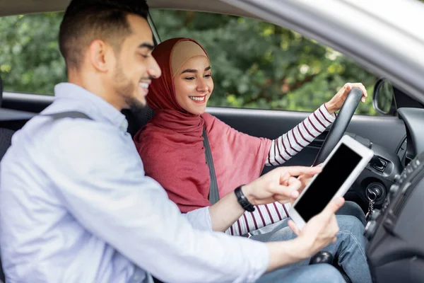 Gelukkig duizendjarig Arabisch man toont weg op tablet naar zijn vrouw in hijab, vrouw met stuurwiel rijden auto — Stockfoto