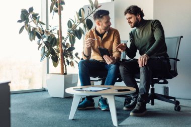 Erkek meslektaşlar tablet bilgisayar kullanıyor, konuşuyor, iş projesinde birlikte çalışıyor, modern ofiste fikirleri tartışıyor.