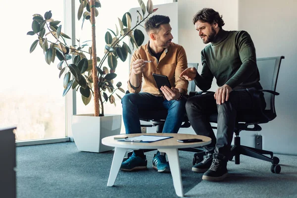 Erkek meslektaşlar tablet bilgisayar kullanıyor, konuşuyor, iş projesinde birlikte çalışıyor, modern ofiste fikirleri tartışıyor.