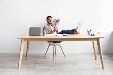 Mutlu adam cep telefonu kullanarak ayaklarını masaya koyuyor.