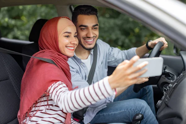 Gelukkig jong moslim vrouw in hijab en echtgenoot rijden met stuurwiel, pauze nemen, selfie maken — Stockfoto