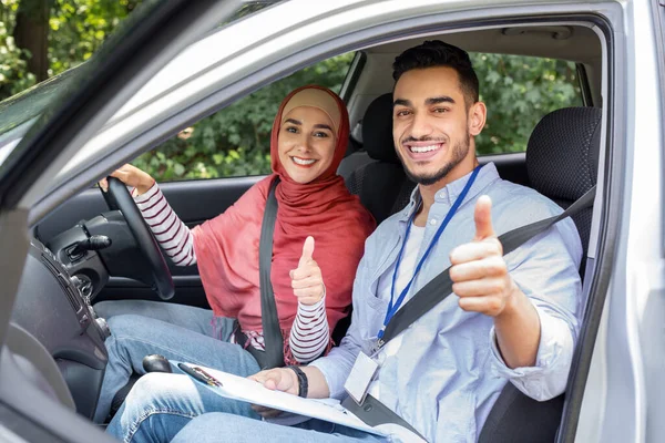 Vrolijke jonge islamitische en vrouw in hijab op stuurwiel in de auto tonen duimen omhoog in cabine auto, buiten — Stockfoto