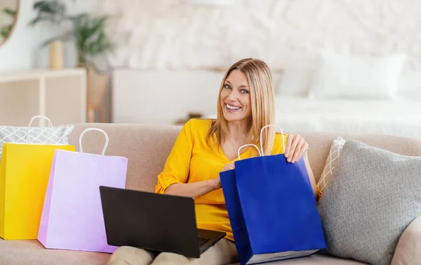 Doymuş genç Avrupalı, sarı elbiseli, laptoplu sarışın kadın alışveriş paketine bakıyor. — Stok fotoğraf
