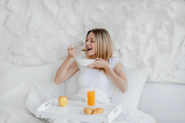 Happy pretty hungry young european blonde woman wake up, have breakfast in white bed — Stok Foto