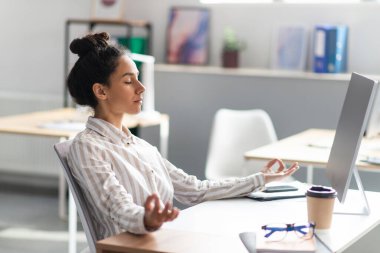 İşte stresle başa çıkmak. Genç Latin ofis çalışanı yoğun bir günün ardından işyerinde meditasyon yapıyor.