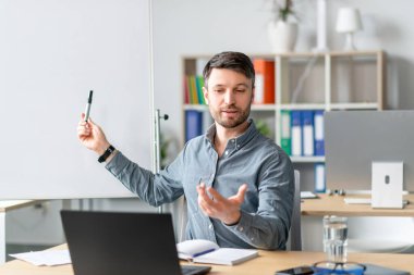 Erkek öğretmen boş karatahtanın yanında uzaktan ders veriyor. Uzaktan eğitim için dizüstü bilgisayar kullanıyor.