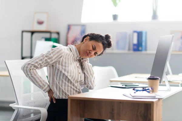 Müde Geschäftsfrau leidet unter Rücken- und Nackenschmerzen, Muskelkrämpfen am Arbeitsplatz im Büroinnenraum — Stockfoto
