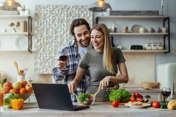 Nöjd tusenårig kaukasisk man med stubb och fru matlagning tillsammans, dricka vin och prata med laptop — Stockfoto