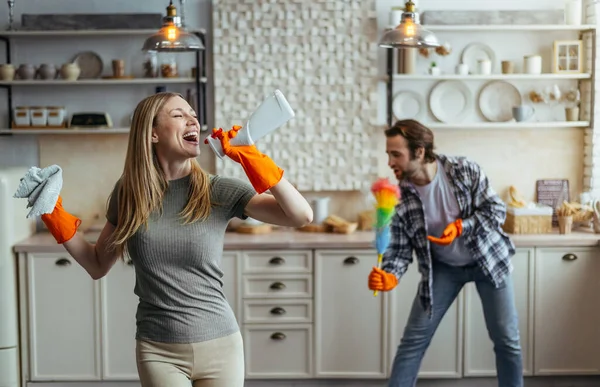 Happy excited millennial caucasian husband and wife in rubber gloves with cleaning supplies sing at imaginary microphone — Stock Photo, Image