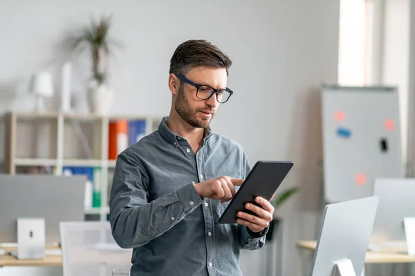 Tecnologías modernas en los negocios. Hombre de negocios maduro concentrado usando tableta digital en la oficina — Foto de Stock