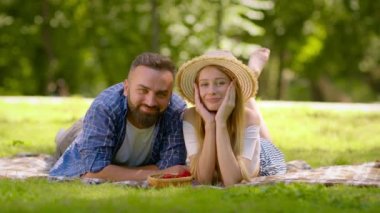 Mutlu bir aile. Yaz parkında çimenlerde dinlenen, piknik yapan ve kameraya gülümseyen pozitif bir çift.