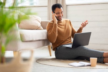 Gülümseyen bir Arap evde çalışıyor ve telefonla konuşuyor.