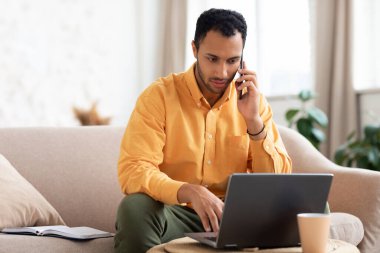 Evde telefonla konuşan ve çalışan odaklanmış bir Arap.