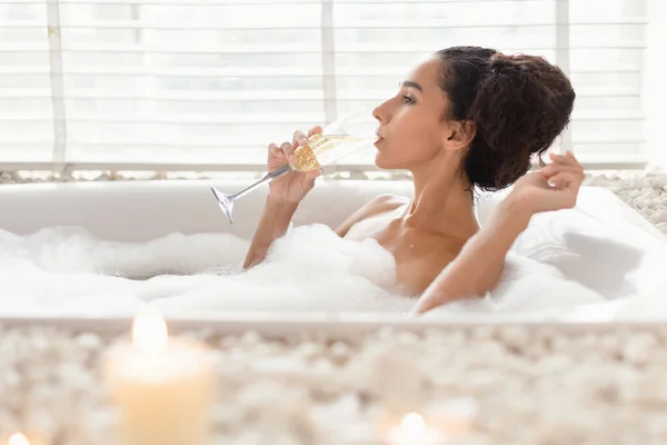 Sexy millennial pani pije szampana leżąc w gorącej kąpieli bąbelkowej w luksusowym hotelu, wolne miejsce — Zdjęcie stockowe