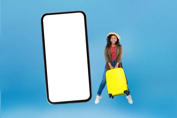 Mujer viajero negro feliz saltando cerca de Smartphone grande, fondo azul — Foto de Stock