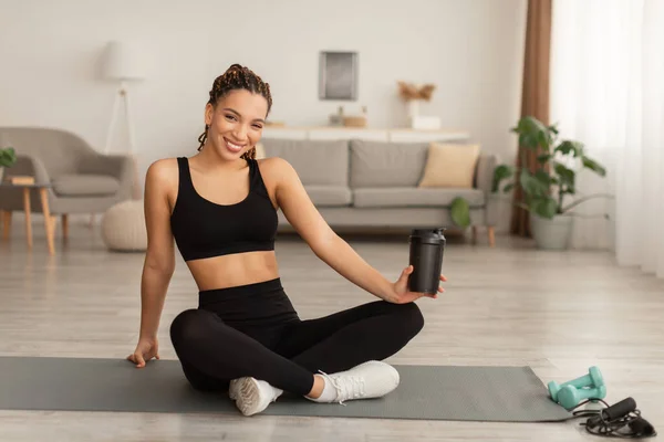 Black Fitness Lady sosteniendo la taza de agua potable durante el entrenamiento en interiores — Foto de Stock