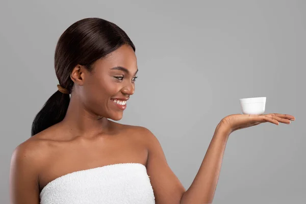 Щаслива красива чорна жінка з ідеальною шкірою тримає банку зволожуючого крему на руці — стокове фото