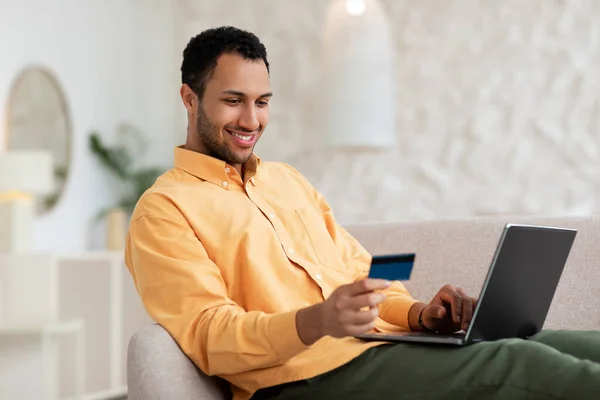 Hombre sonriente casual usando PC y tarjeta de crédito en casa —  Fotos de Stock
